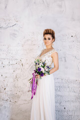 beautiful girl bride blond girl in white dress with gold decorations with wedding bouquet makeup and hair in the Studio looking at the camera profile, white background