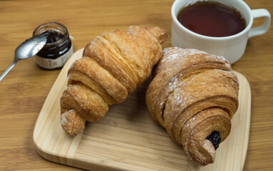 Delicious fresh croissants with fruit jam and tea on wooden