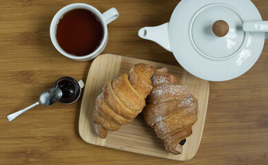 Delicious fresh croissants with fruit jam and tea on wooden