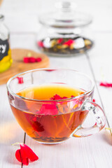 A cup of tea, in the background of a bank with a black herbal floral tea on a white wooden table.