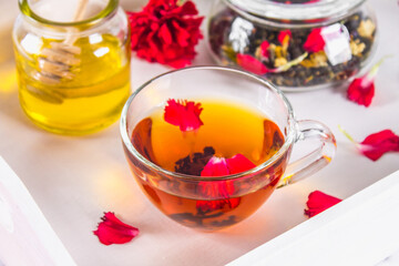 A cup of tea, a can of honey and a jar of black herbal tea on a white tray in bed.