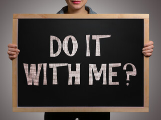 Girl (student, businesswoman) in casual clothes holding a black chalk board with text Do it with me?