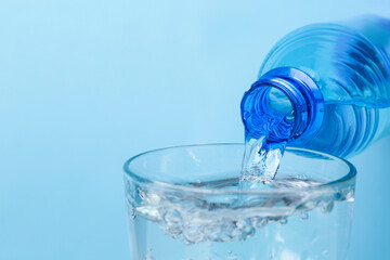 Water pouring from bottle into glass on color background