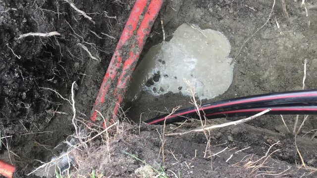 Electrical cable being buried in a large hole with other communication cables; camera pans up to wooden spool at end.  