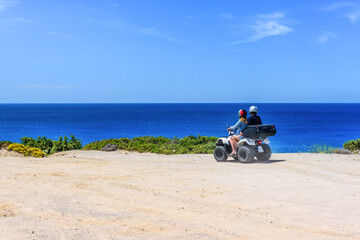 Young couple on a quad during trip along coast of Milos island, Greece.