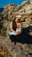 mum holding baby boy on the sea playing and breastfeeding