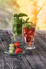 Strawberries and grapes on a skewer on the glass background with strawberry and grape detox drink on a wooden table on a Sunny day. The vertical frame. Selective focus.