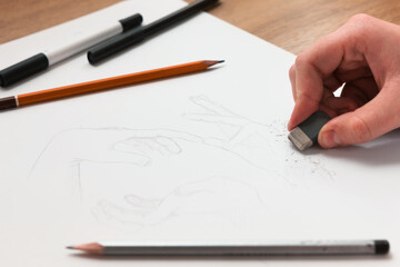 From above hand erasing lines on a sketch. Horizontal indoors shot. Drawing lessons, art school, young artist concept