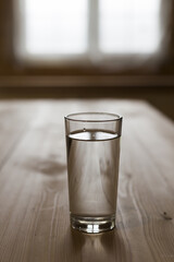 Glass of water on wooden table with blurred window behind