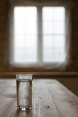 Glass of water on wooden table with blurred window behind