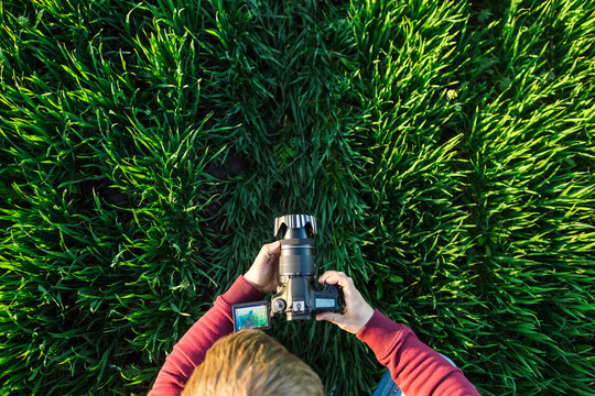 fascinating photography and process of shooting concept - male man takes photos on a digital camera with LCD display on field of green grass, top view on head, arms and equipment