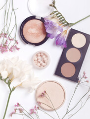 Makeup products surrounded by pink and white flowers on white background. Flat lay. Top view