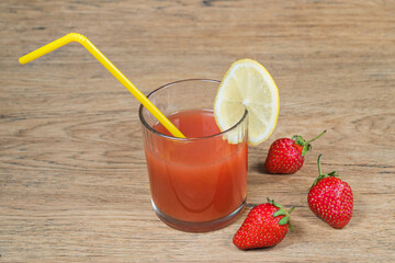 Fresh strawberry juice with a slice of lemon on a glass next to strawberries on an old wooden table