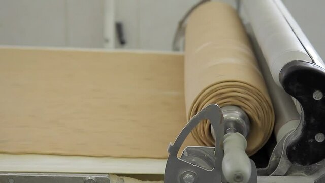 Dough twist in roll around special equipment on conveyor in bakery factory. Beige plastic assembly line with ribbed surface moving very fast, on one side there is roller covered with flour with white