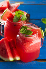 Tasty fresh appetizing watermelon drink smoothie with mint on blue table. Closeup.