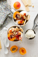 Tasty fresh cold appetizing vanilla ice cream with nuts, apricots, waffles and syrup on white table with ingredients for making dessert. Top View.