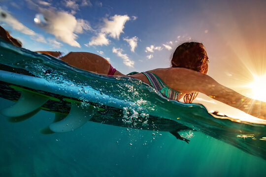 Surfer girl paddling on a board at sunset