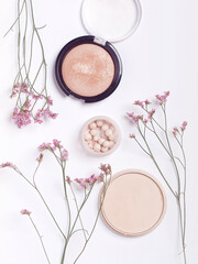 Makeup products surrounded by small pink flowers on white background. Flat lay. Top view