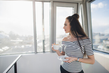 Smiling young businesswoman holding a coffee cup and looking out the window.