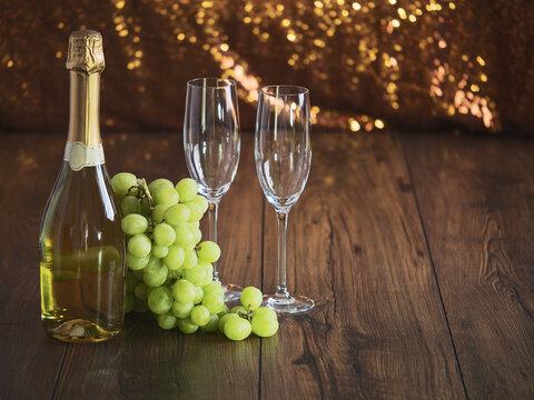 Two flutes bottle of champagne and cluster of grapes on a wooden , sparkling bokeh in the background.