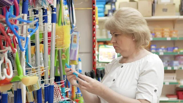 Elderly woman chooses cleaning accessories in the supermarket. Shopping in the store. Senior female carefully analyzing products in a market. Shopping in Store or Supermarket