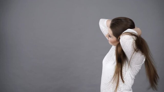 Woman combing her healthy hair with comb. Young latin female with beautiful natural brown straight long hairs -studio shot on grey background 4K ProRes HQ codec