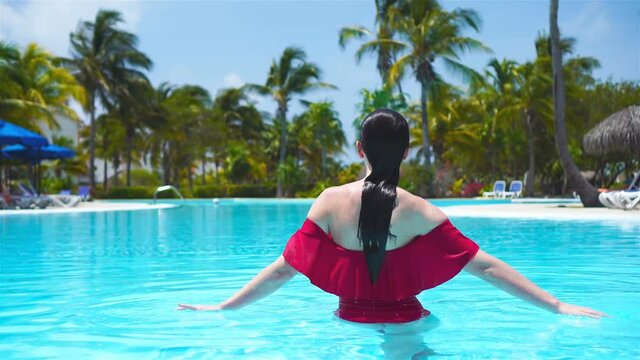 Beautiful young woman relaxing in swimming pool. Happy girl in outdoor pool at luxury hotel