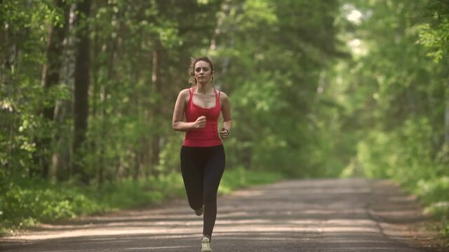 young woman Jogging in summer forest. the girl goes in for sports in the nature. the model runs towards the camera.