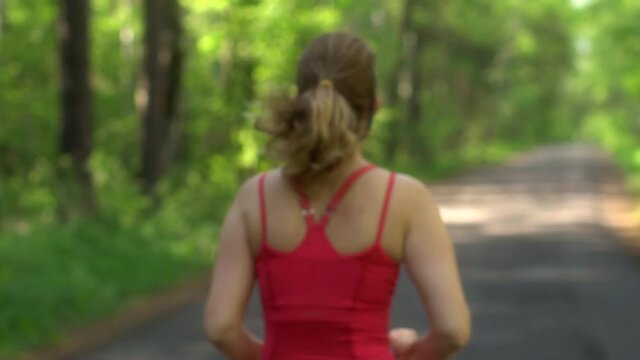 young woman Jogging in summer forest. the girl goes sports in the nature. back athletes bokeh. slow motion