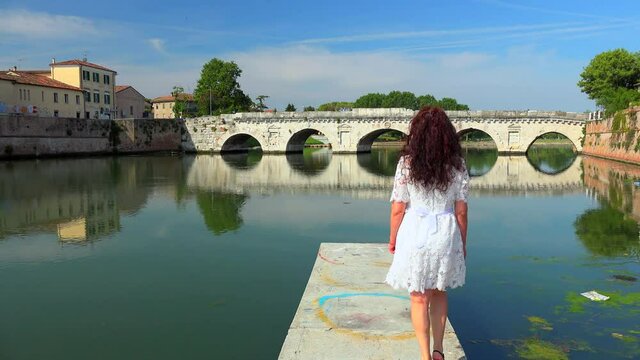 mature woman coming on pier on quiet water with ancient Roman bridge in the background