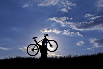 Fototapeta premium silhouette of a cyclist with a raised bike in the sun.