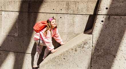 Fototapeta na wymiar amazing closeup view of happy, joyful smile little girl hiking on concrete wall on sunny spring day