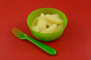 Canned Bartlett pear slices in green plastic bowl with plastic fork on red wood table