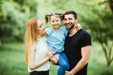 Fototapeta premium Happy young family spending time together in green nature. wife with husbend and daughter. Mother and father holding daughter in park