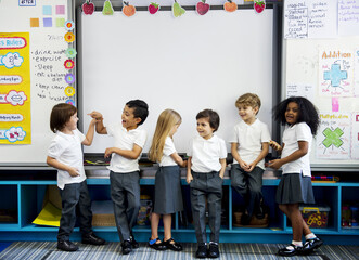 Group of diverse kindergarten students standing together in classroom - obrazy, fototapety, plakaty