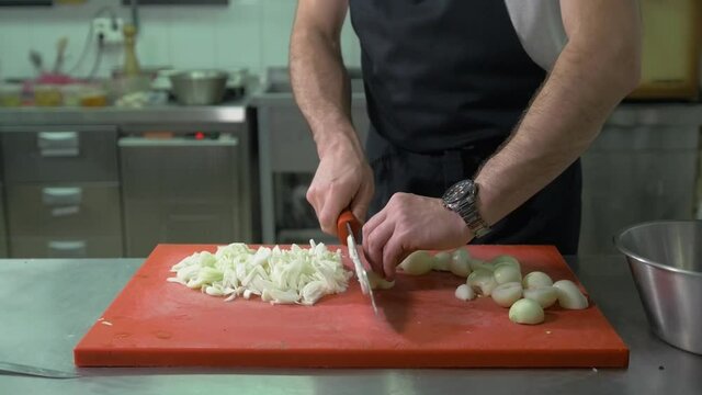 Chef chopping a red onion with a knife on the cutting board in restaurant kitchen