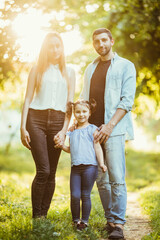 Fototapeta premium Happy mother, father and daughter in sunset in summer park
