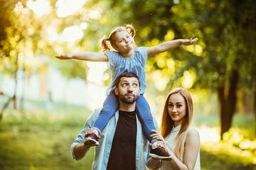 Fototapeta premium Happy family playing in nature late afternoon sunlight in the fall, summer. Mother, father and daughter playing on the grass in the park, laughing and smiling, fun, joy.