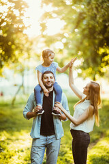 Fototapeta premium happy family Mom and Dad holding daughter on his back and have fun in the park.