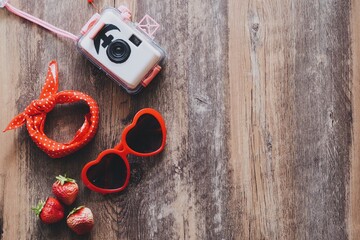 Red sunglasses on wooden table with strawberry and polka dot towel and camera on wooden table,summer concept red theme