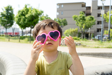 ハートのサングラスをかけた男の子がスイーツを楽しむ夏の屋外ポートレート｜家族レジャー・お祭りイメージに最適な子ども写真