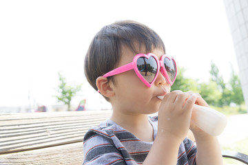 ハートのサングラスをかけた男の子がスイーツを楽しむ夏の屋外ポートレート｜家族レジャー・お祭りイメージに最適な子ども写真