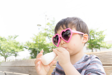 ハートのサングラスをかけた男の子がスイーツを楽しむ夏の屋外ポートレート｜家族レジャー・お祭りイメージに最適な子ども写真