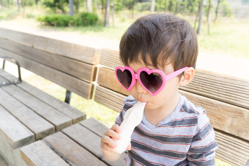 ハートのサングラスをかけた男の子がスイーツを楽しむ夏の屋外ポートレート｜家族レジャー・お祭りイメージに最適な子ども写真