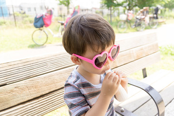 ハートのサングラスをかけた男の子がスイーツを楽しむ夏の屋外ポートレート｜家族レジャー・お祭りイメージに最適な子ども写真
