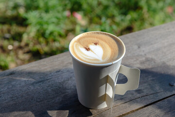 Paper cup of coffee on wooden table at the garden, copy space background