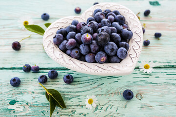 Tasty and fresh forest blueberries in a heart shaped bowl on wooden table.