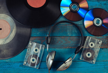 Vinyl records, CDs, audio cassettes, headphones are laid out on a blue wooden surface. Top view. 80s.