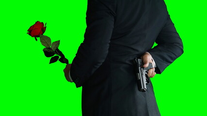 Businessman isolated on green screen. A man or killer in black suit with a black gun in and a red rose his hands.