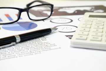 side view and selective focus ball pen and number pad calculator placed on graph paper with blurred glasses for accountant; financial; risk analysis concept.